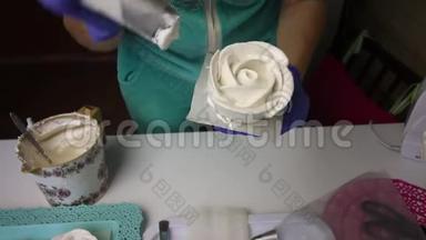 一个女人使用糕点袋和喷嘴形成玫瑰花瓣从棉花糖。 把完成的棉花糖从看台上移走